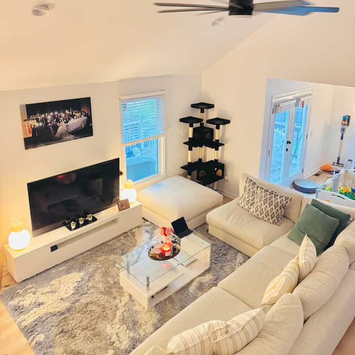 Bright beige and white toned living room featuring a large sofa, cat tower, and baby playpen creating a cozy atmosphere