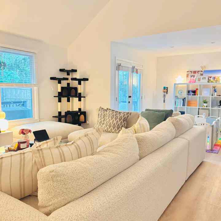 Bright white-toned living room featuring a large cream sectional sofa and a black cat tower, creating a cozy atmosphere