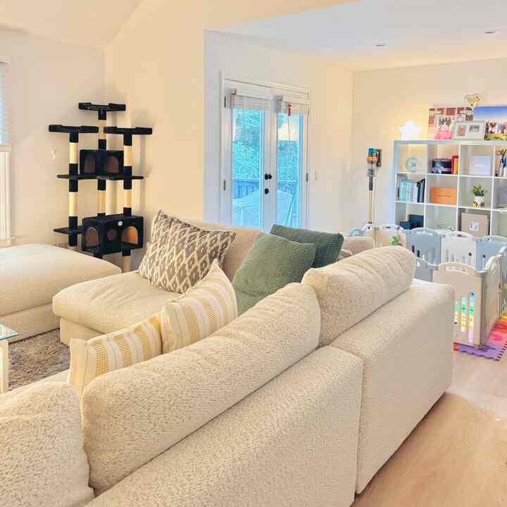 White-walled living room with natural-toned sofa, featuring a baby playpen and cat tree, cozy and functional space