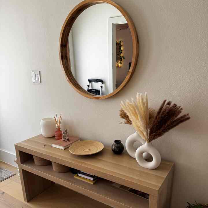 Wood tone and white entrance space featuring a round wooden mirror and console table with minimalist vases and decorations creating a cozy atmosphere