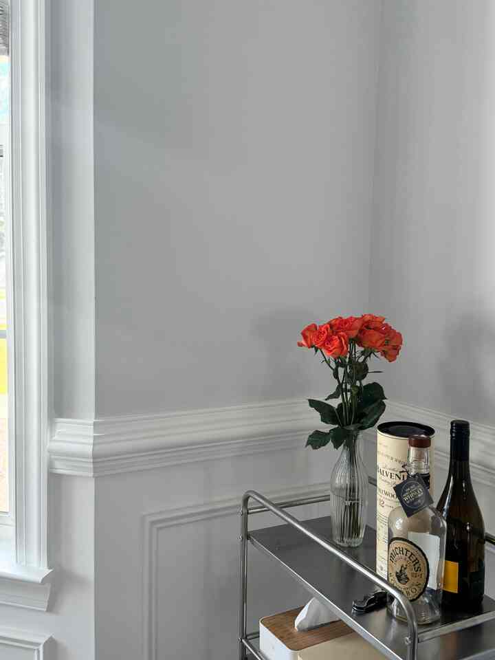 White corner room with molding featuring a metal bar cart and a vase of orange flowers, simple and clean home bar space