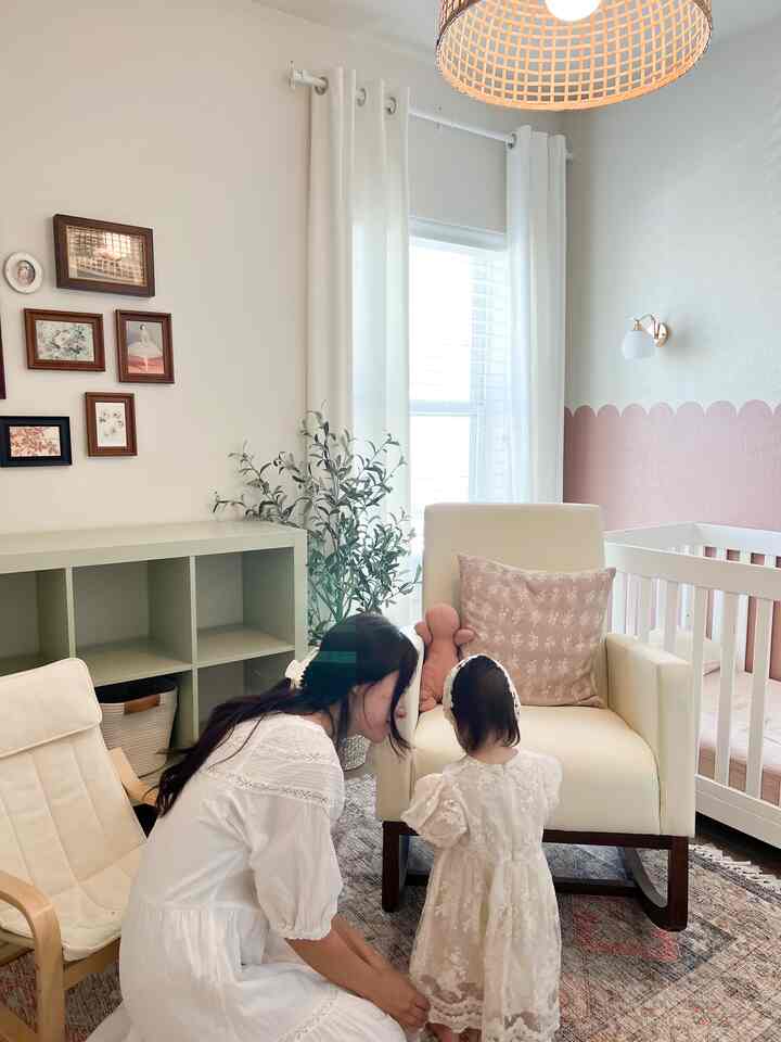 Pink and white toned nursery featuring a crib and armchair in a warm and cozy setting
