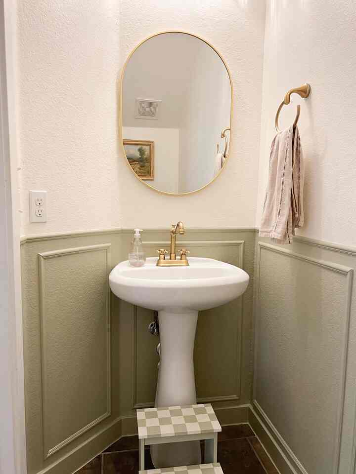 White and natural color bathroom featuring a gold faucet and oval mirror in a cozy space