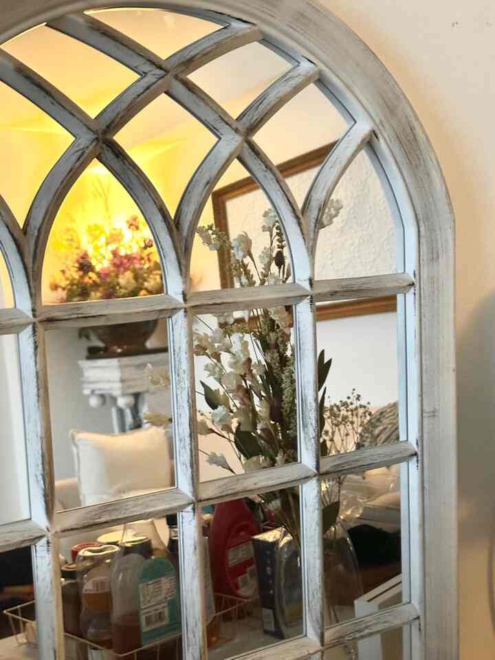Warm beige and white toned indoor space featuring an arch mirror reflecting flowers and kitchen items, creating a calm atmosphere
