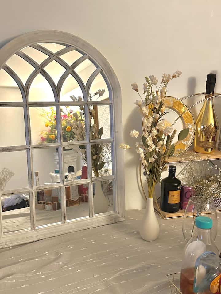 White and yellow toned living room featuring an arch mirror and vases with dried flowers in a cozy French Country style