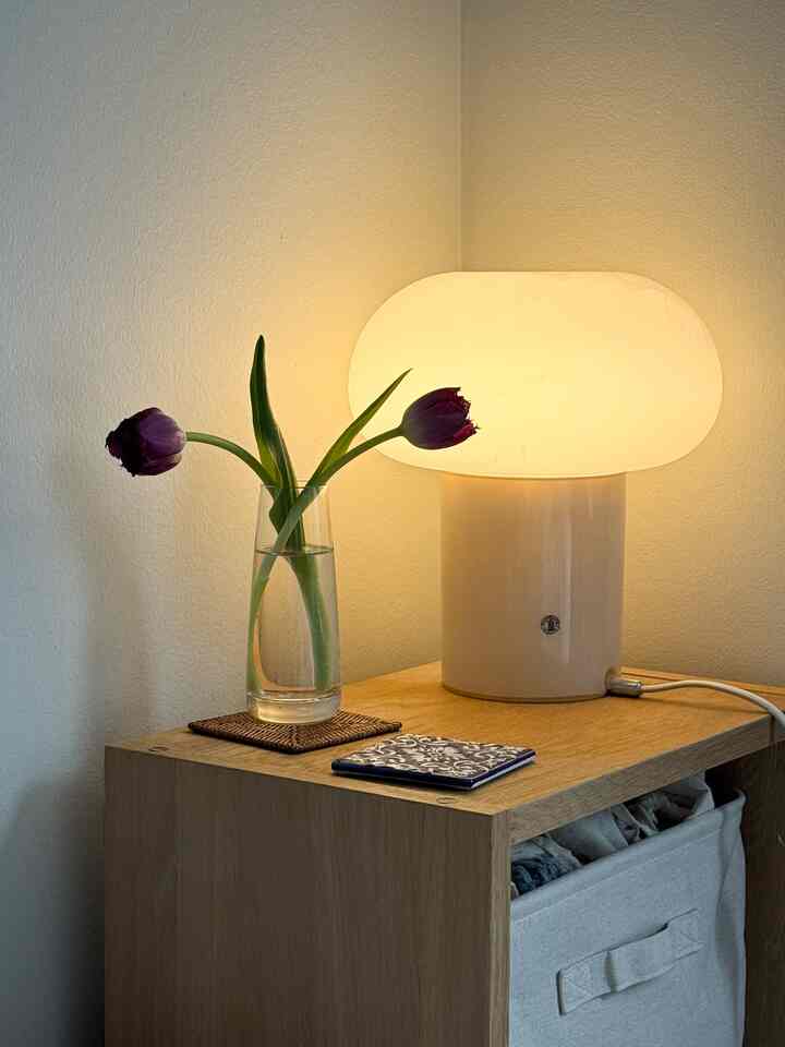 Beige-toned nightstand featuring a vase with flowers and a table lamp in a simple warm setting