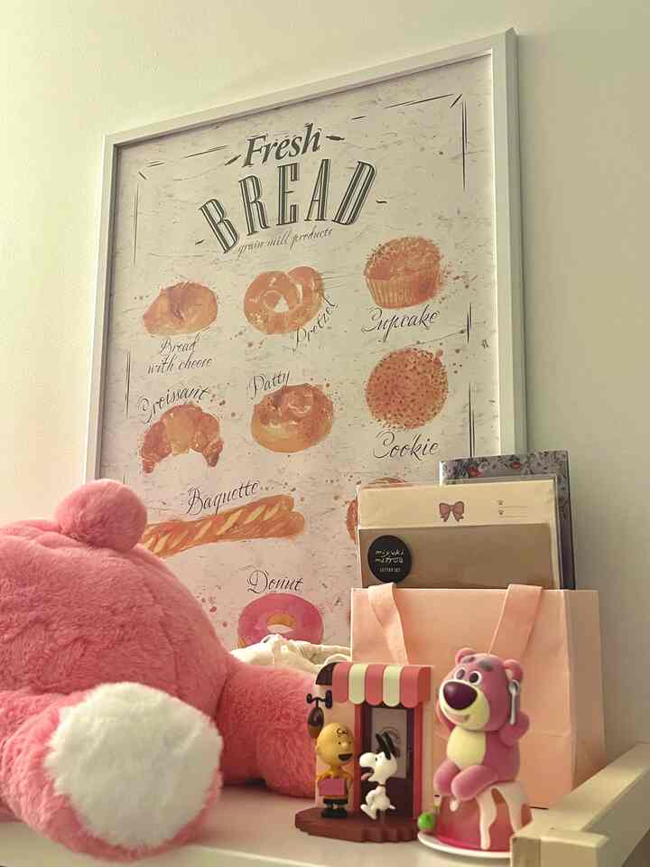 Cozy apartment interior with pink plush toy and large bakery-themed framed art on simple bookshelf