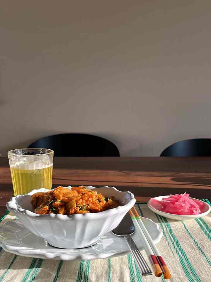 Modern dining table with white plates and kimchi fried rice on a green-striped placemat, featuring chopsticks and glass