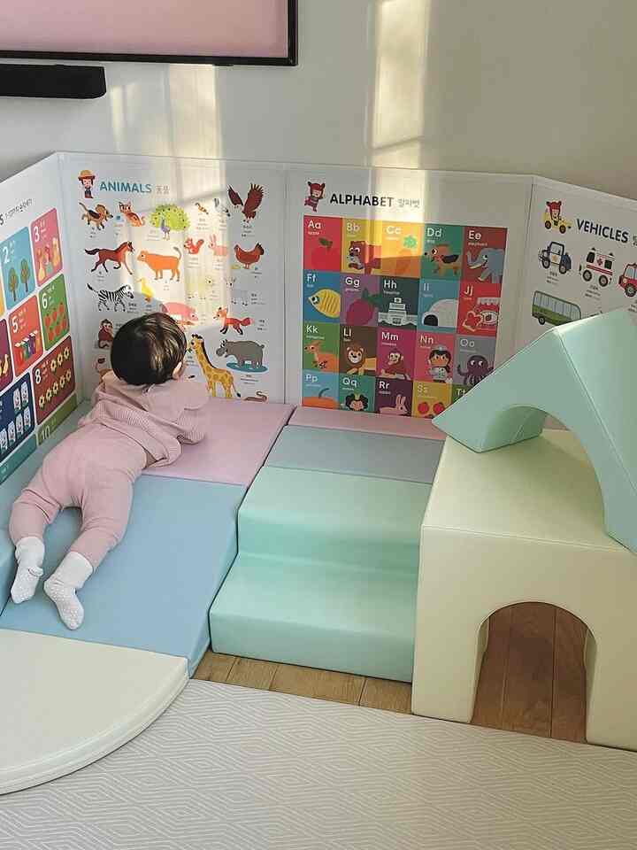 Pastel-toned kids’ play area in living room featuring a toddler on a multifunctional foam play set surrounded by educational wall posters