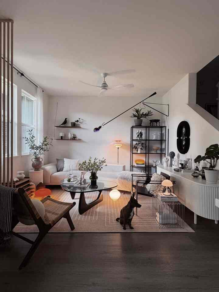 A cozy mid-century modern living room with white walls and sofa, brown flooring and chairs, complemented by plants and a dog