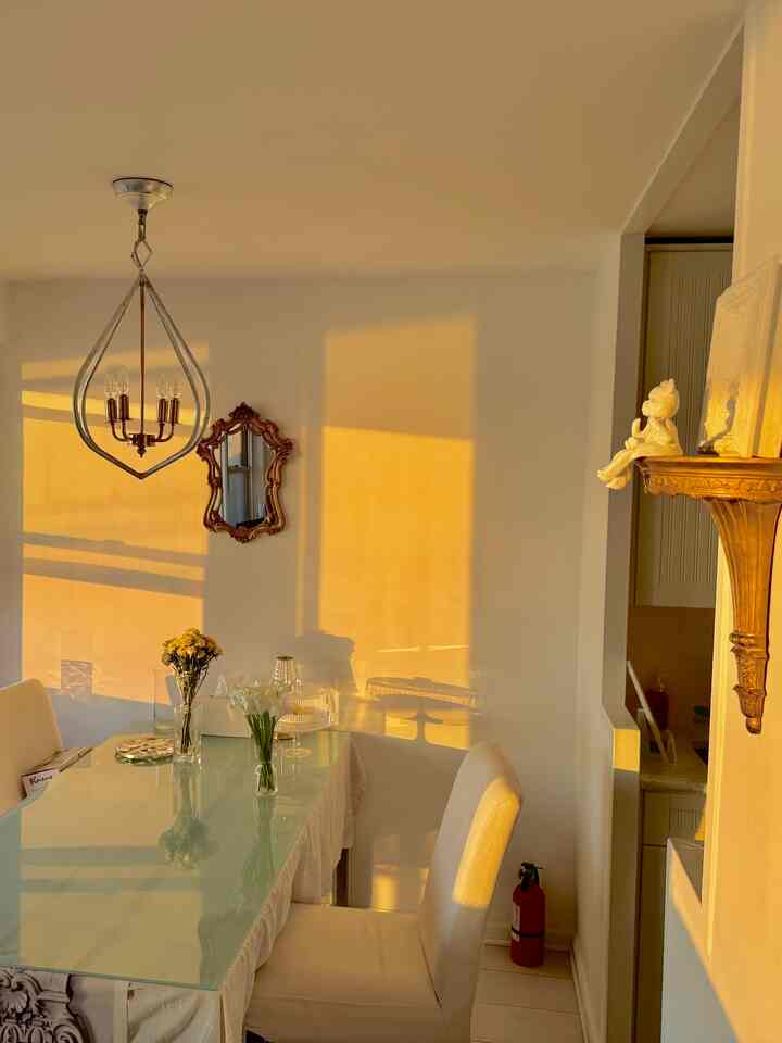 White dining room with gold-tone pendant light, featuring a glass dining table and white chairs in a warm ambiance
