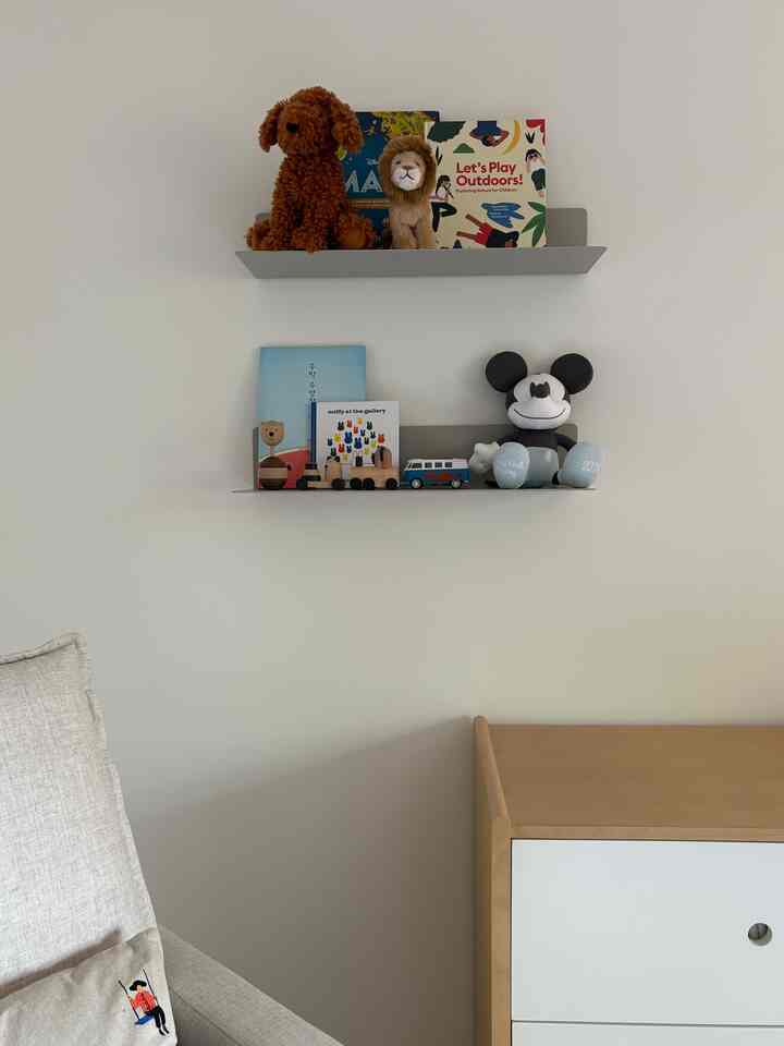 Bright wood tone and white-walled Scandinavian-style kids' room featuring wall shelves with toys and books, and a cozy dresser