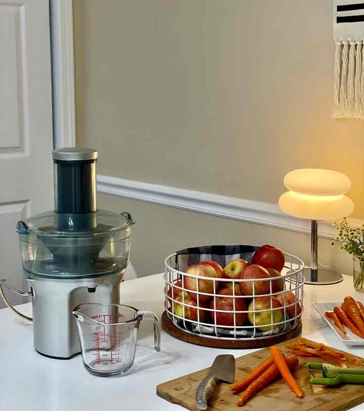 Beige-toned kitchen featuring white table, juicer, fresh apples and carrots arranged in a cozy setting
