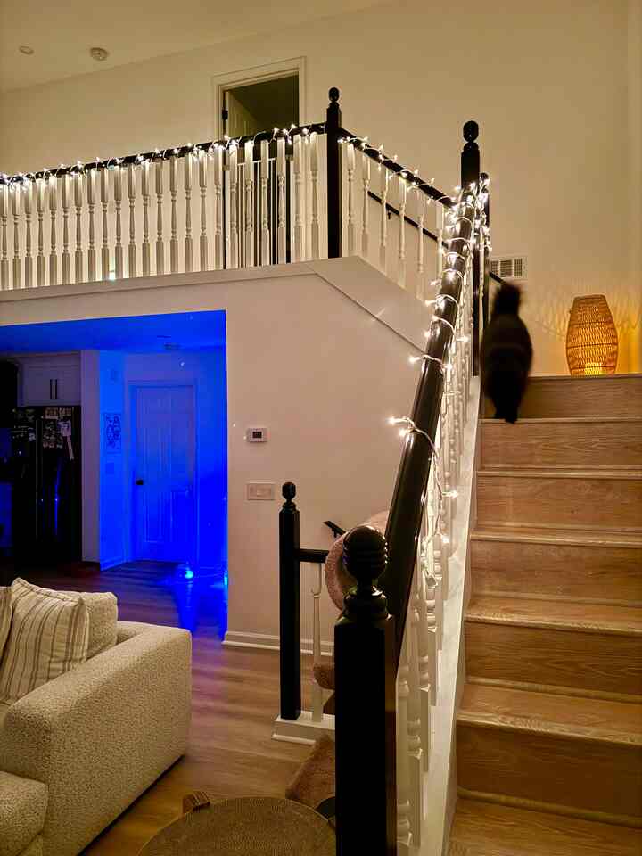 Cozy living room and stairs space with wood tones and white colors, featuring a cat and string lights decoration