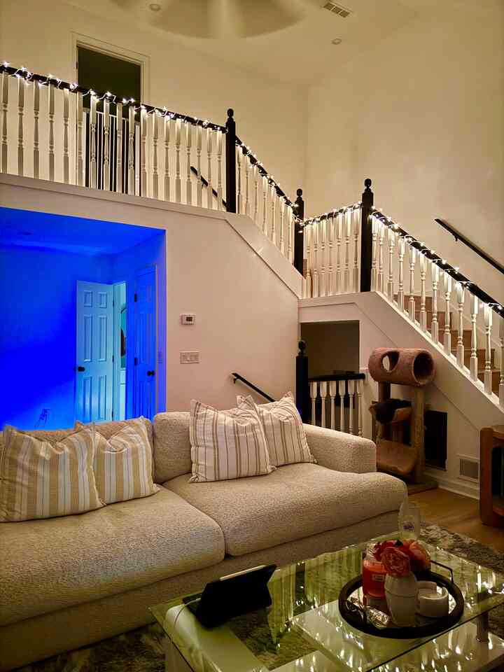 Natural-toned living room featuring a beige sofa and string lights draped along stair railing, creating a cozy ambiance