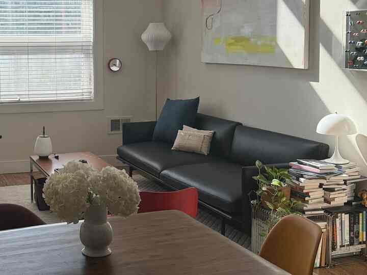 Living room with white walls and black leather sofa, featuring natural elements and a cozy reading area