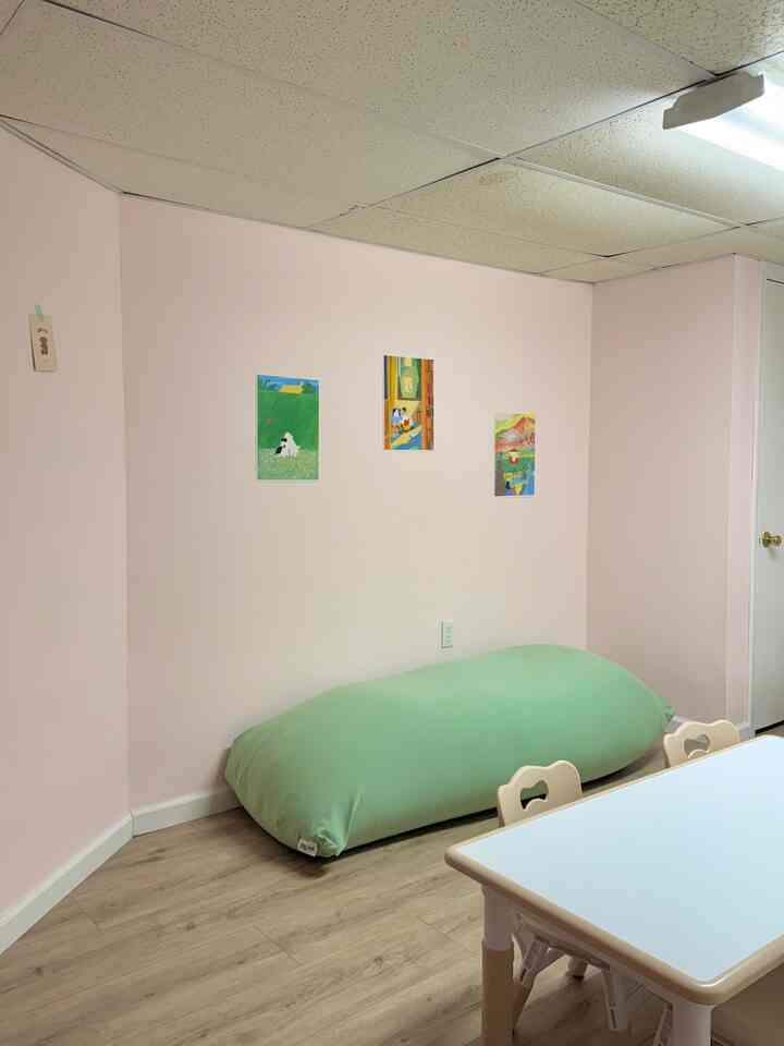 Light pink walls and wood flooring feature a kids' room with a white table, chairs, and a large green bean bag creating a cozy space