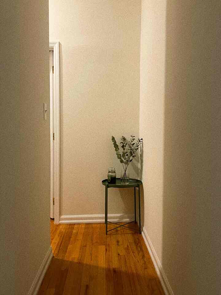 Warm wood tone floor and walls featuring a green tray side table with candle and plant in a cozy narrow space