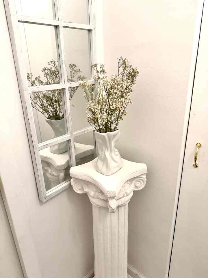 White-toned corner space featuring window pane mirror and paper bag style vase on classic pedestal with cozy interior vibe