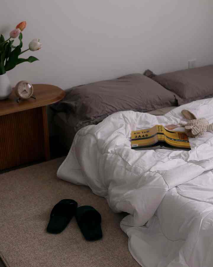 White and brown tone bedroom featuring a nightstand with a vase of flowers and a clock, creating a cozy atmosphere