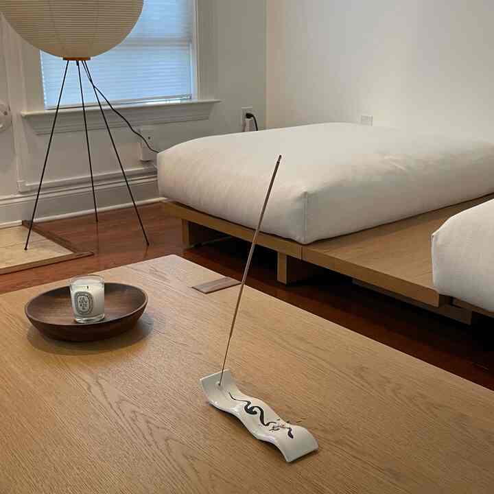 A minimalist bedroom with white and wood tones, featuring a wooden table with incense and candle creating a cozy atmosphere