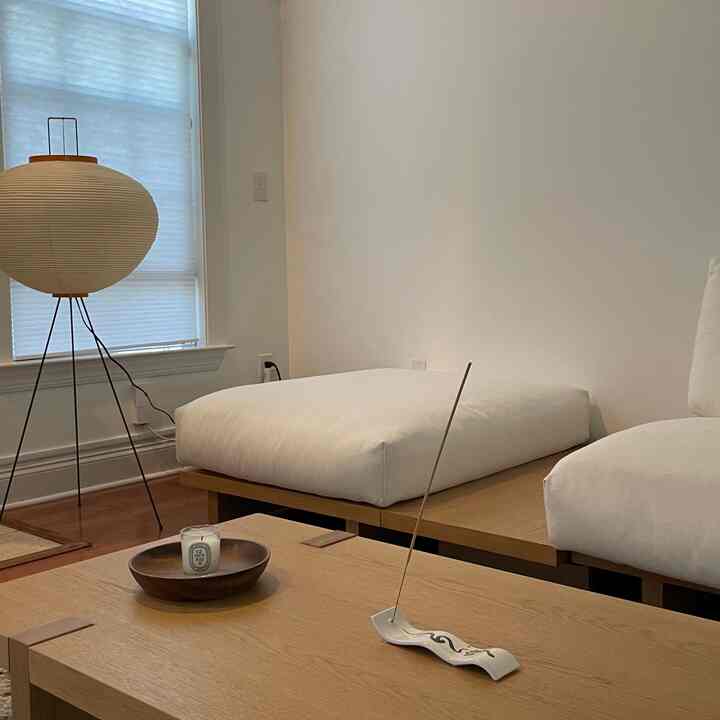 A simple and serene living room in white and wood tones featuring a sofa, coffee table, and lit incense for a soft scent ambiance