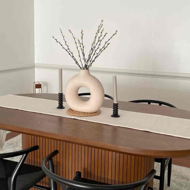 Natural tone dining room with white walls, wood tone dining table featuring a simple table runner, vase with branches, and candles
