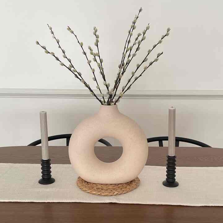 Natural beige and brown toned dining room featuring a ceramic vase and candle holders on a neat table runner at center
