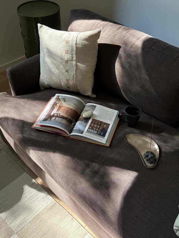 Beige and brown toned home office featuring a sofa bed with an open book and a cup, creating a cozy reading corner