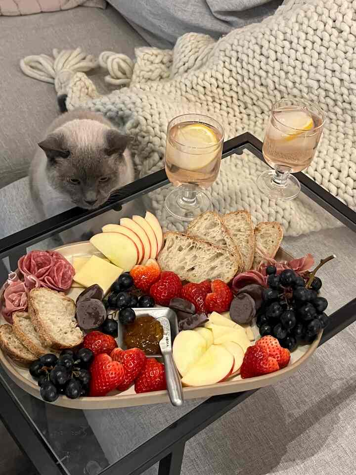 White and gray toned living space featuring a glass-top coffee table with snacks and two drinks, a cat sitting to the left, creating cozy atmosphere