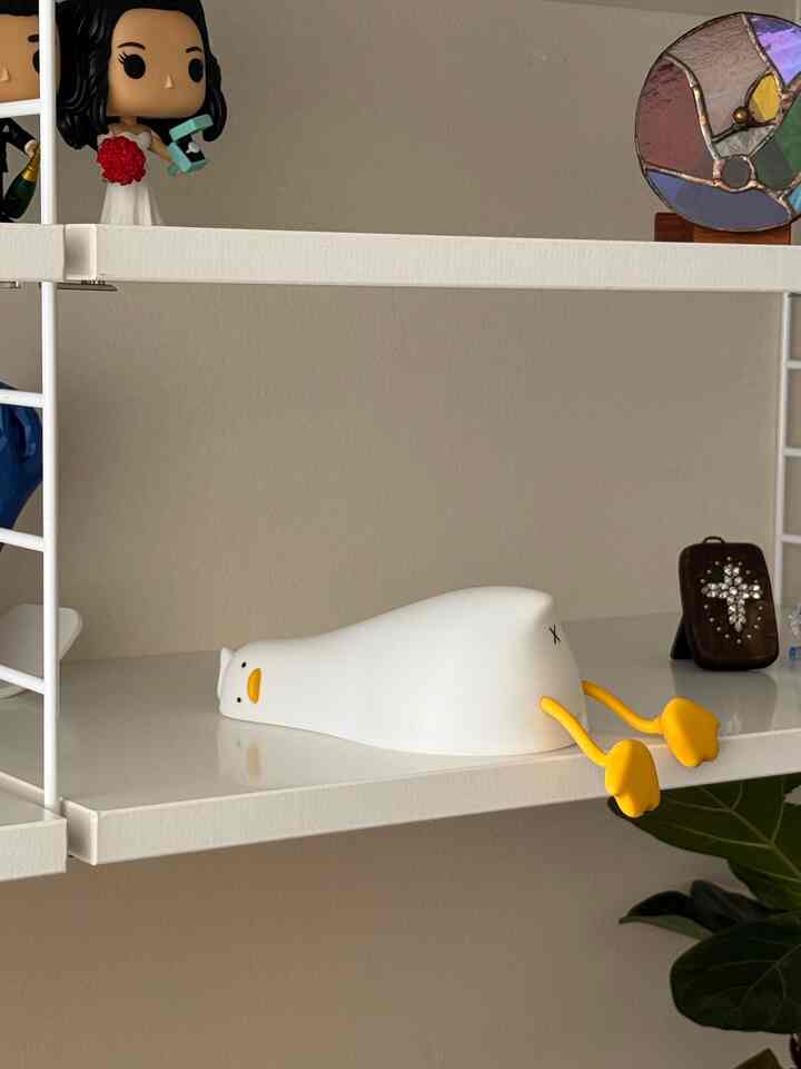 Clean space featuring a white and yellow duck night light lying flat on a white shelf with various decorative objets