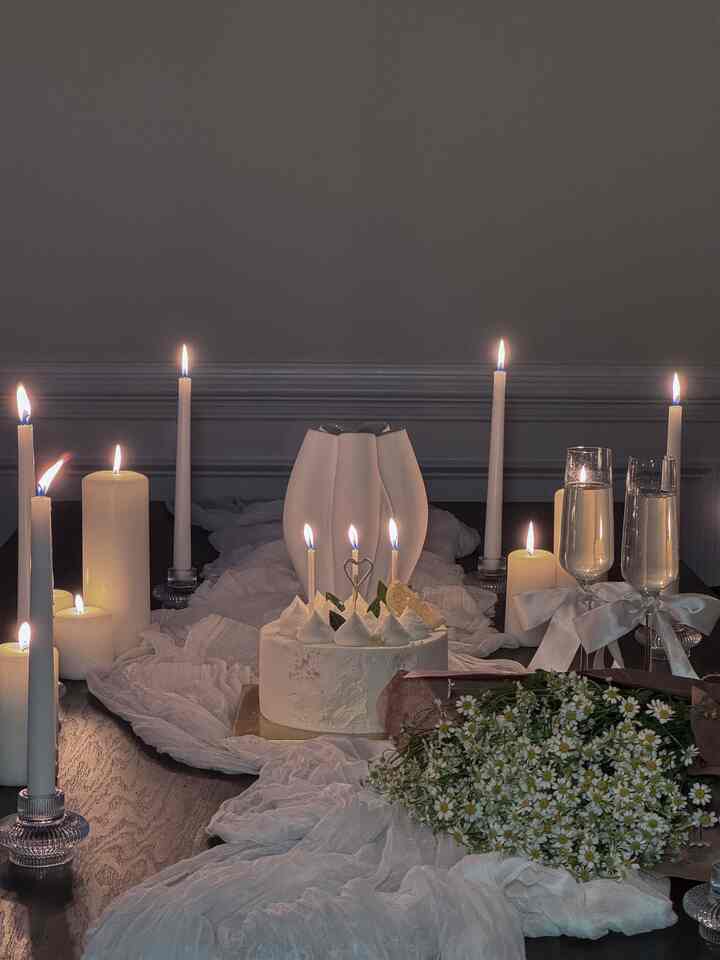 Soft white-toned dining room featuring a table setting with lit candles and birthday cake creating a cozy ambiance