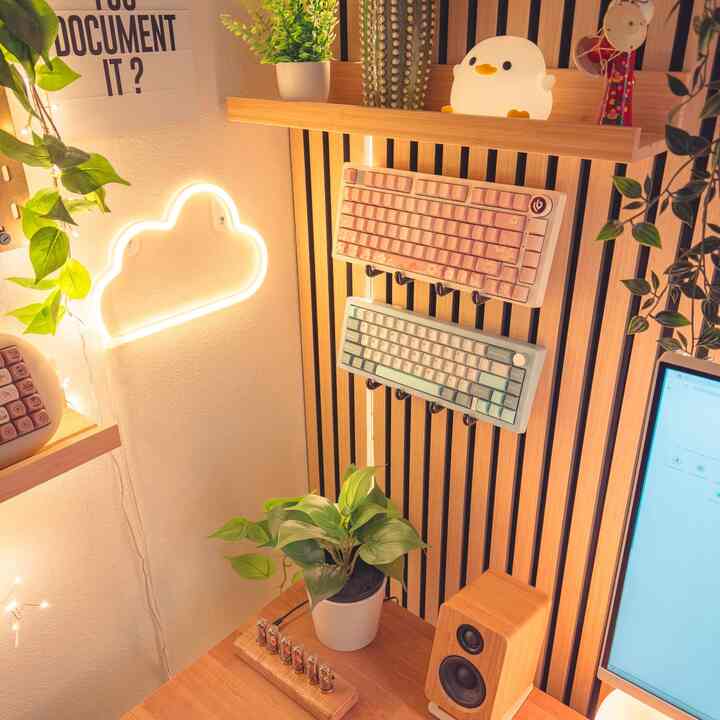 Cozy home office with warm wood tones and green plants, decorated with cloud neon sign and mechanical keyboards