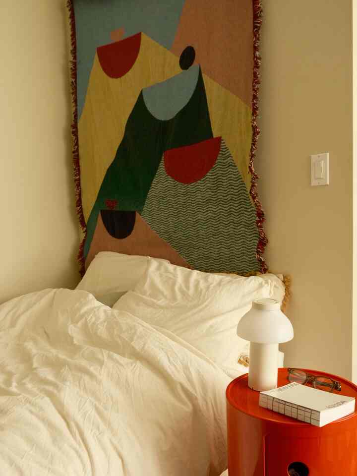 Natural tone bedroom featuring white bedding, red nightstand, and table lamp in a cozy atmosphere
