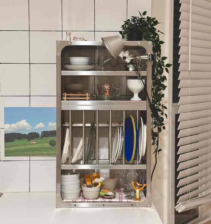 Minimal kitchen space with white tiled walls and stainless steel kitchen rack featuring organized plates and cups