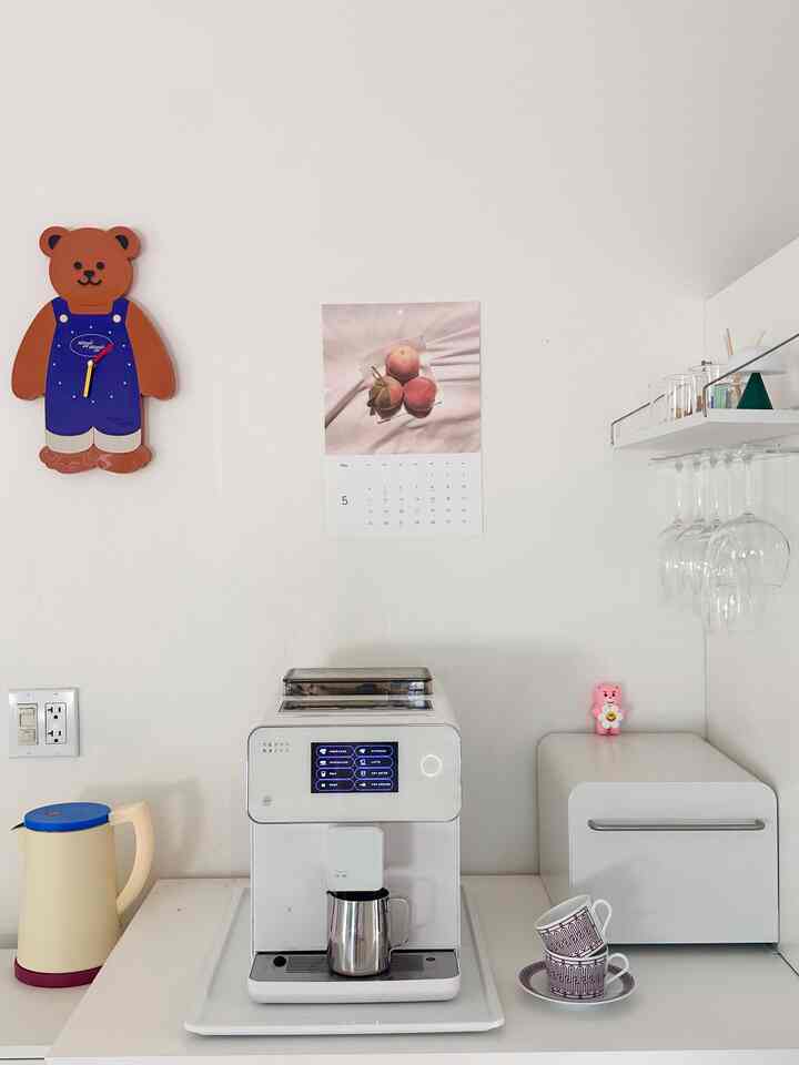 White-toned kitchen space featuring a central espresso machine and coffee accessories with a minimal and simple interior