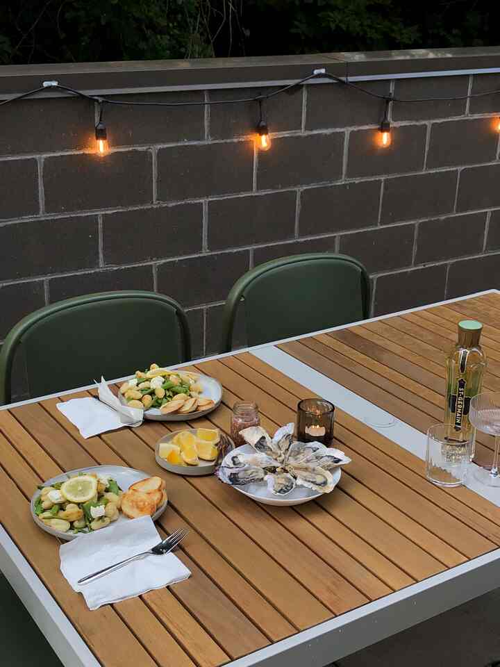 Beige-toned outdoor space featuring wooden table, green chairs, and string lights creating a cozy home party atmosphere