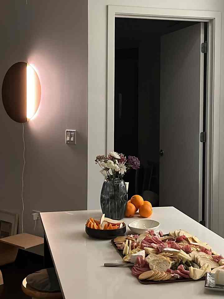 Beige walls and white table in living room featuring vase with flowers and food platters, creating a home party atmosphere