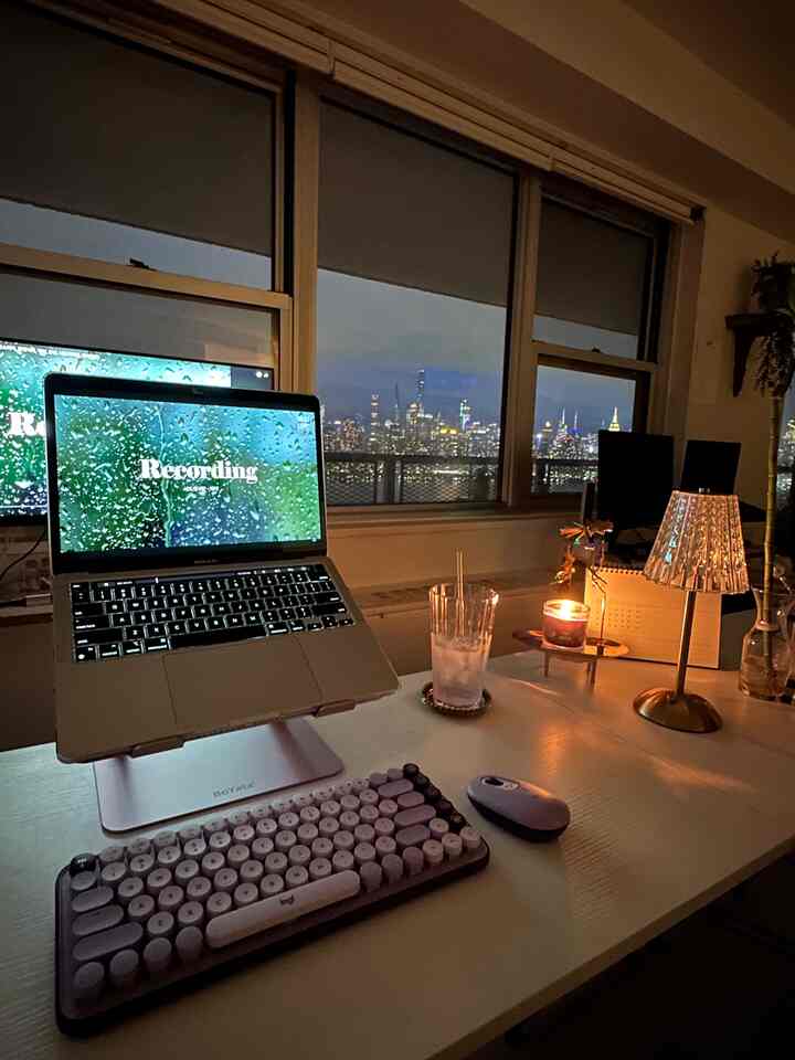 Cozy home office with white desk, warm lighting, and city skyline visible through large window at night