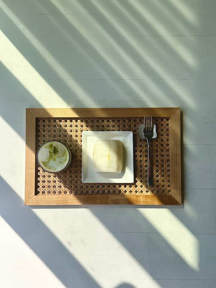 Simple home cafe setting with wood tone rattan tray, cutlery, and transparent glass on white background