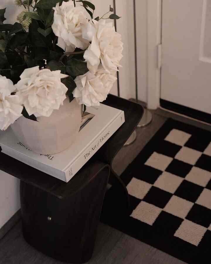 Black and white toned entrance space featuring a dark coffee table with a white vase and flowers arranged neatly