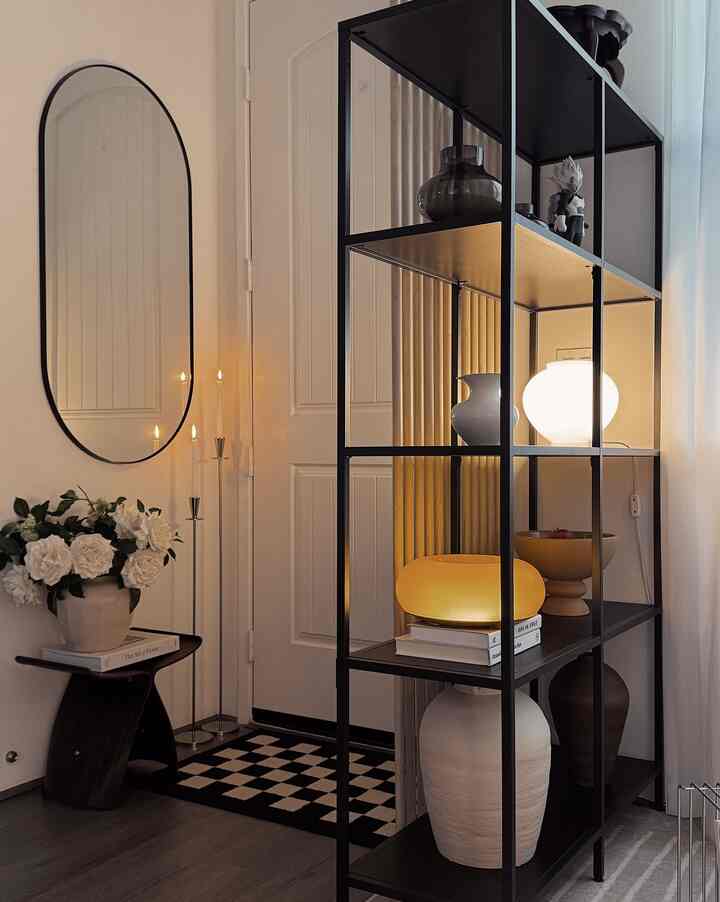 Modern entrance space featuring black metal shelving and a tall oval mirror with warm ambient lighting
