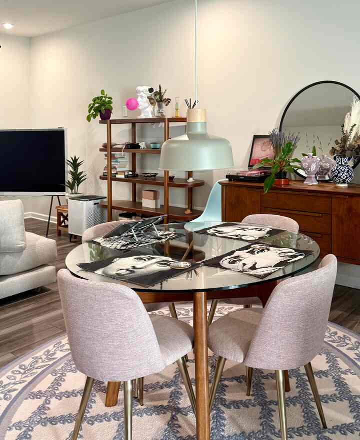 Bright white walls with brown wood furniture, a round glass dining table with pink dining chairs in a modern natural 4-person dining room