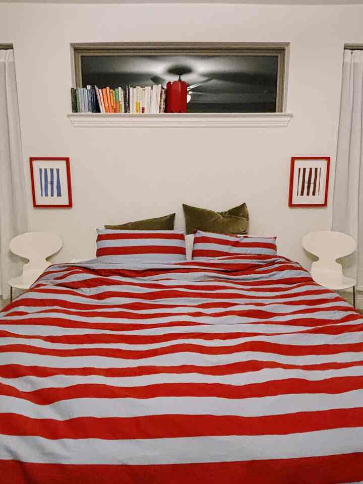 Red and white toned bedroom featuring a bed with striped bedding center and white chairs flanking both sides, creating a clean aesthetic