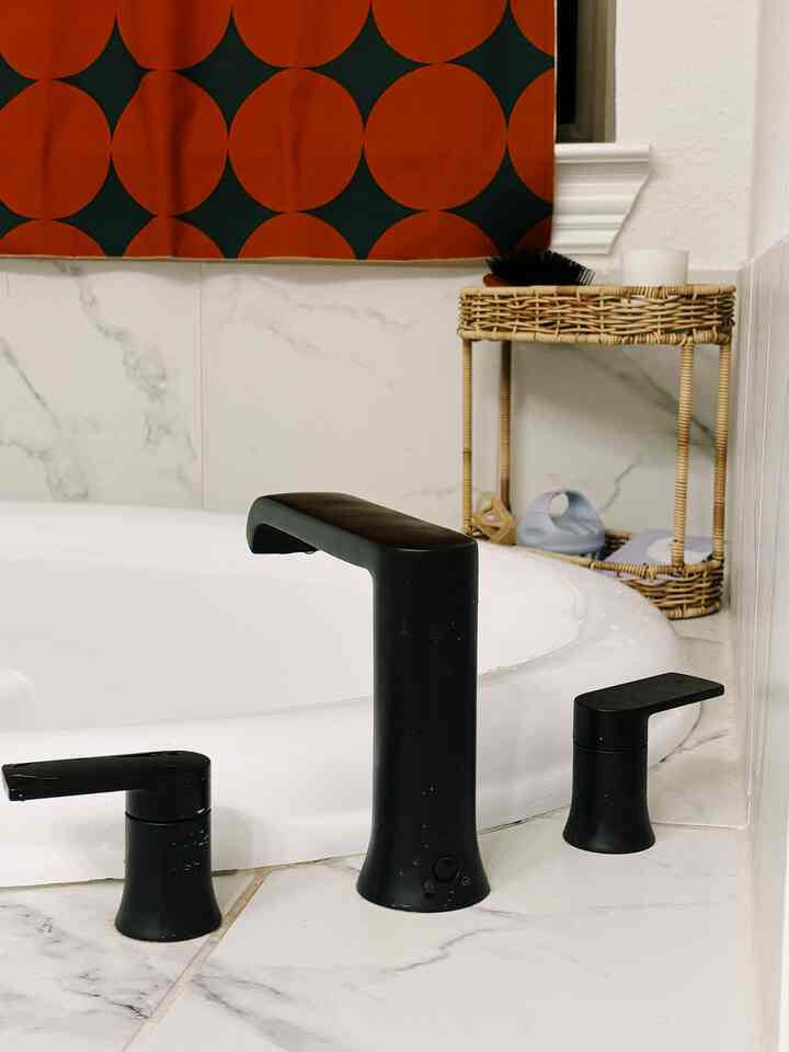 White and black toned bathroom featuring marble tiles, matte black faucet set, and natural woven tray in a clean modern space