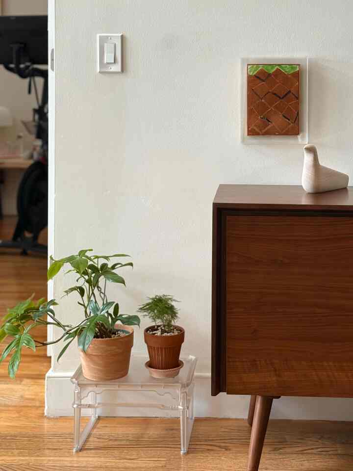 Natural modern corner space with white walls and wood tone furniture featuring a transparent stool and terracotta plant pots, creating a clean atmosphere
