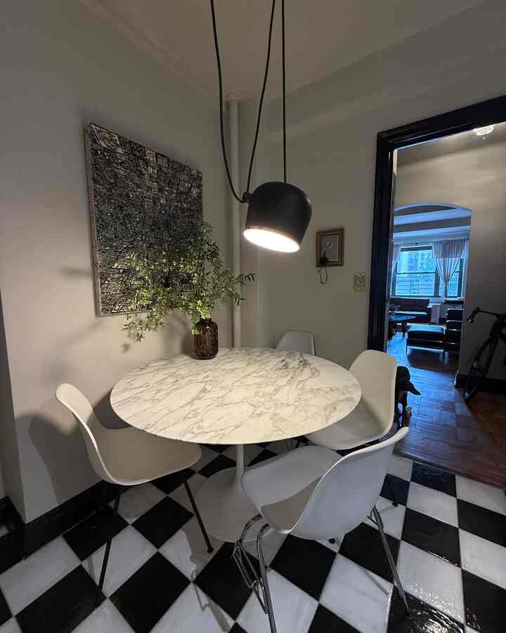 Small dining room in white and black tones featuring a round marble dining table, pendant light, and white dining chairs arranged around