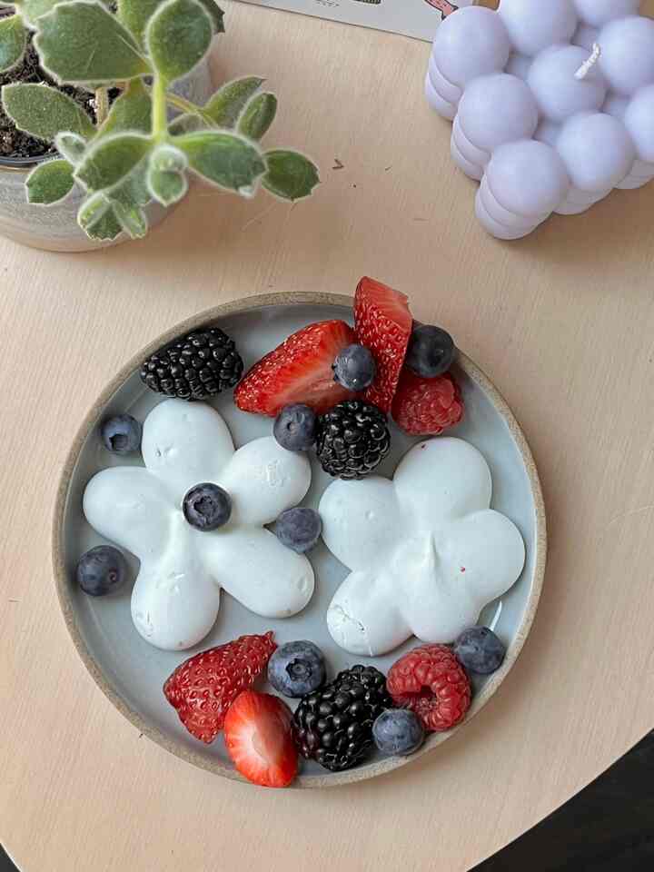 Bright, warm wooden table featuring a Hasami porcelain plate with flower-shaped meringues and fresh berries in a cozy atmosphere