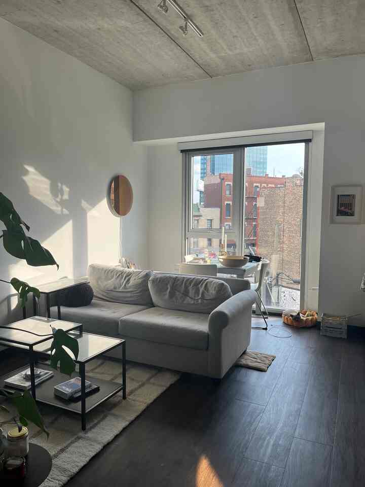 White and natural toned living room featuring a simple gray sofa, glass coffee tables, and a cat bed by the window in a minimalist space