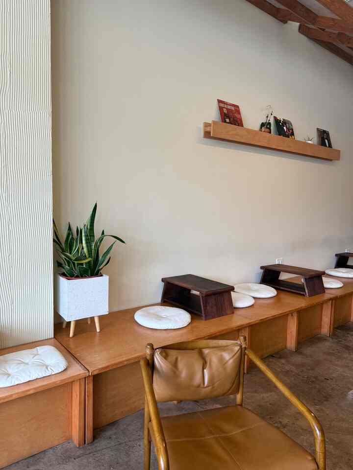 Natural-toned room with wooden bench seating, leather armchair, and plant, creating a cozy cafe-style atmosphere